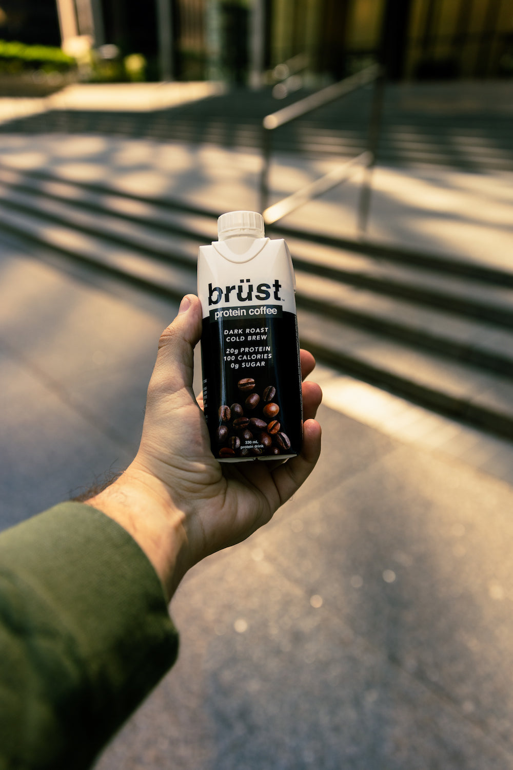 hand holding a brüst unsweetened dark roast protein cold brew coffee bottle outdoors