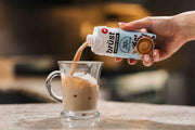 pouring brüst french vanilla protein cold brew coffee over ice in a glass mug